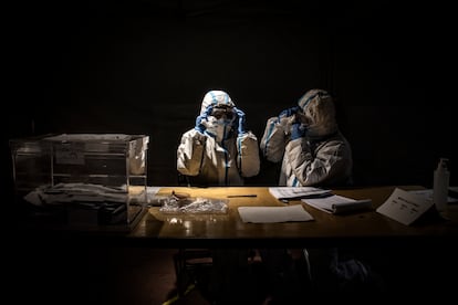 Dos trabajadores electorales con equipo de protección esperan a los votantes en un colegio electoral durante las elecciones regionales catalanas el 14 de febrero de 2021, en Barcelona.