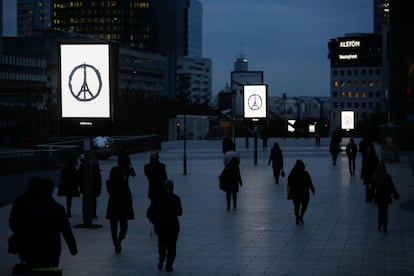 Gente camina junto a carteles publicitarios en los que se muestra la 'Paz para París' en el distrito financiero de La Defensa en París (Francia). Los parisinos han regresado a sus trabajos este lunes ante la mirada atenta de policías y soldados armados.