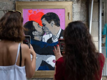 Dos mujeres fotografían la obra del artista urbano Salvatore Benintende, donde Pedro Sánchez y Pablo Iglesias se dan un beso, en Barcelona.