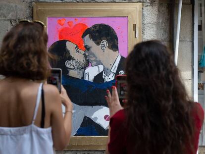 Dos mujeres fotografían la obra del artista urbano Salvatore Benintende, donde Pedro Sánchez y Pablo Iglesias se dan un beso, en Barcelona.