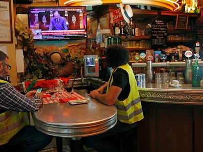 Dois coletes amarelos ouvem Philippe na televisão na quarta-feira, em um bar em Paris.