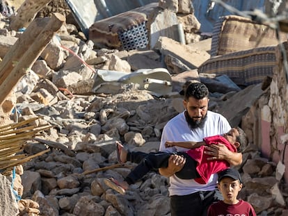 TOPSHOT - A man carries a boy as he walks past destroyed houses after an earthquake in the mountain village of Tafeghaghte, southwest of Marrakesh, on September 9, 2023. Moroccans on September 10 mourned the victims of a devastating earthquake that killed more than 2,000 people, as rescue teams raced to find survivors trapped in the rubble of flattened villages. (Photo by Fadel SENNA / AFP)