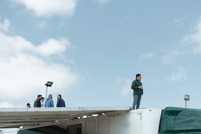 Un hombre observa desde lo alto de su camión un evento automovilístico mientras otros hombres hablan entre ellos.