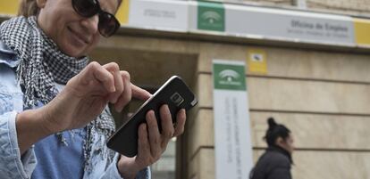 Una mujer usa un móvil en la puerta de una oficina de empleo en Sevilla.