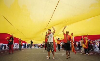 Manifestantes luciendo banderas de España bajo una bandera gigante.