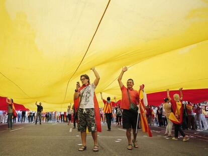 Manifestantes luciendo banderas de España bajo una bandera gigante.