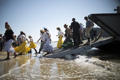 Varias mujeres vestidas de rociera, saltan al agua desde la rampa del barco que las ha cruzado desde Sanlúcar de Barrameda hasta Doñana.