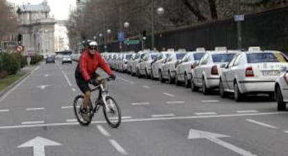 Un ciclista pasa ante una fila de taxis aparcados junto a la valla de El Retiro, en la calle Alfonso XII, en Madrid. EFE/Archivo