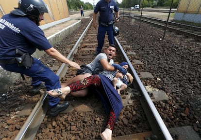 Policiais húngaros tentam tirar uma família de refugiados dos trilhos do trem, na estação de Bickse, na Hungria.