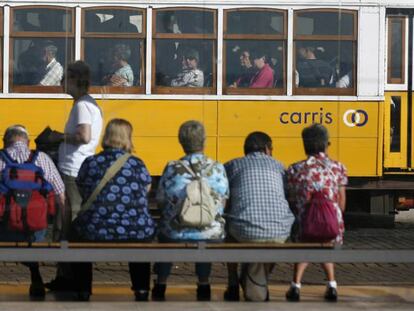 Várias pessoas aguardam em uma parada de bonde elétrico em Lisboa.