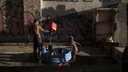 Homem banha crianças em uma favela do Rio de Janeiro.