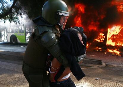 Una joven es detenida frente a uno de los dos autobuses ardiendo.