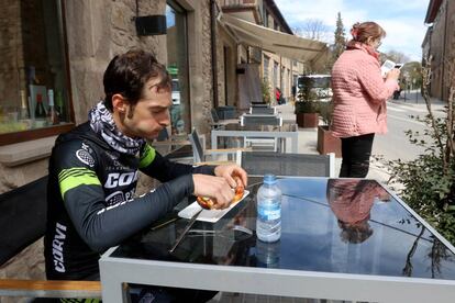 Un ciclista almuerza y una señora consulta el móvil a la espera de que pase la Volta por Perafita.