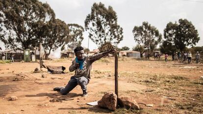 Un manifestante utiliza un tirachinas para lanzar una piedra a los miembros de la policía antidisturbios en Suráfrica.