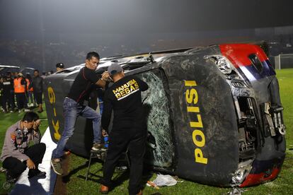 Tras la derrota por 2-3 del equipo local —la primera vez que caía ante su archirrival en más de dos décadas, según AFP— cerca de 3.000 seguidores del Arema FC invadieron el campo y los agentes trataron de dispersar a los aficionados con cargas y lo que parecen gases lacrimógenos. En la imagen, agentes examinan un vehículo dañado dentro del estadio.