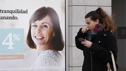 Una  mujer pasea delante de una publicidad de ahorro de un banco. 