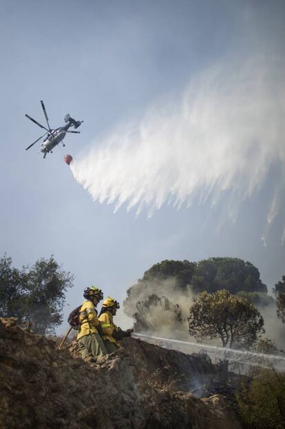 Miembros del Infoca intentan apagar el incendio con la ayuda de un helicóptero, en la localidad onubense de Nerva.