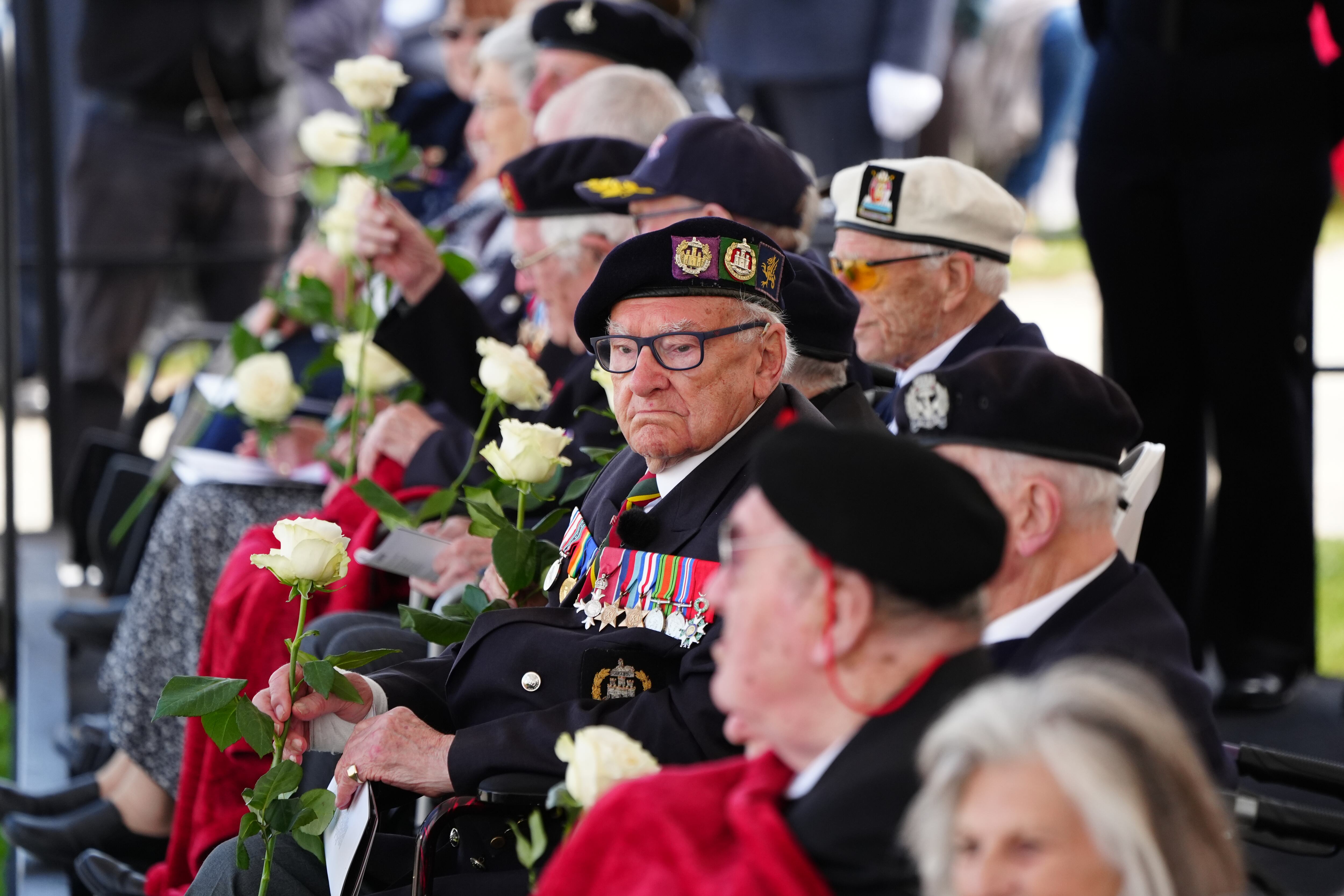 Veteranos de guerra sosteniendo rosas que recibieron de escolares durante el evento conmemorativo nacional del Reino Unido, celebrado en el Memorial Británico de Normandía en Ver-sur-Mer (Francia).