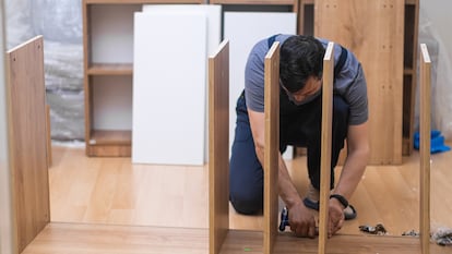 Un hombre atornillando un mueble.