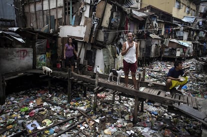 Un grupo de personas sobre un puente de madera que cruza un canal lleno de residuos en Manila (Filipinas).