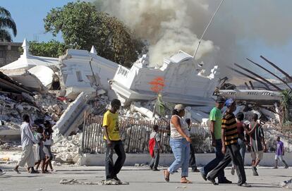 Un grupo de personas camina junto a las ruinas en llamas del ministerio de justicia pocos días después del terremoto (16/01/2010)