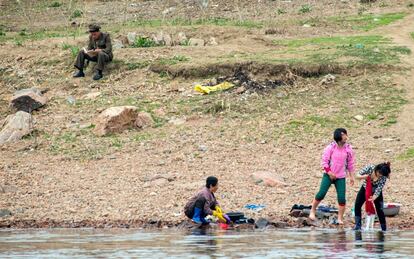 Un soldado norcoreano lee un libro al lado de tres mujeres que lavan ropas en el Río Yalu.