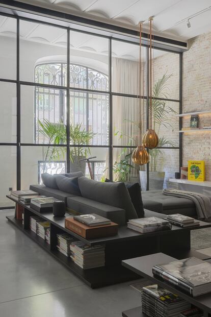 La diseñadora alemana Kirsten Schwalgien, residente en la capital catalana y conocedora del legado modernista, se encargó de convertir este espacio diáfano, que originalmente servía como cochera, en una vivienda. En la imagen, las ventanas industriales protegen la sala acústica y visualmente. La lámpara colgante es de Vanessa Mitrani. El sofá de Minotti se envuelve con aparadores de castaño ahumado.