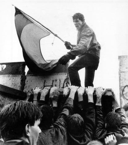 Um manifestante segura uma bandeira da Alemanha Ocidental enquanto seus companheiros atiram uma seção do Muro, perto do Portão de Brandemburgo, no sábado após a queda. O bloco de cimento foi recolocado por agentes fronteiriços orientais.