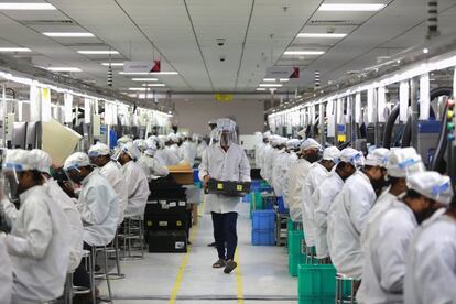 Empleados protegidos con máscaras trabajan en la producción de teléfonos móviles, en Noida (India).