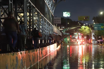 Personas buscan superar la inundación de Circuito Interior pasando por una de las bardas de la línea 5 del metro.