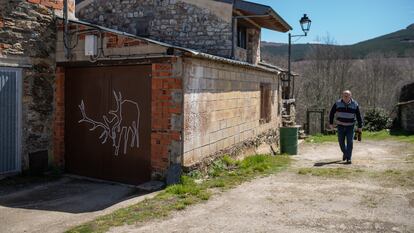 Un vecino de Linarejos pasa junto a una puerta pintada con la silueta del ciervo Carlitos.