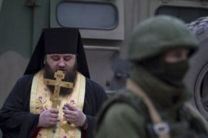 Un pope reza junto a un uniformado en Balaclava.