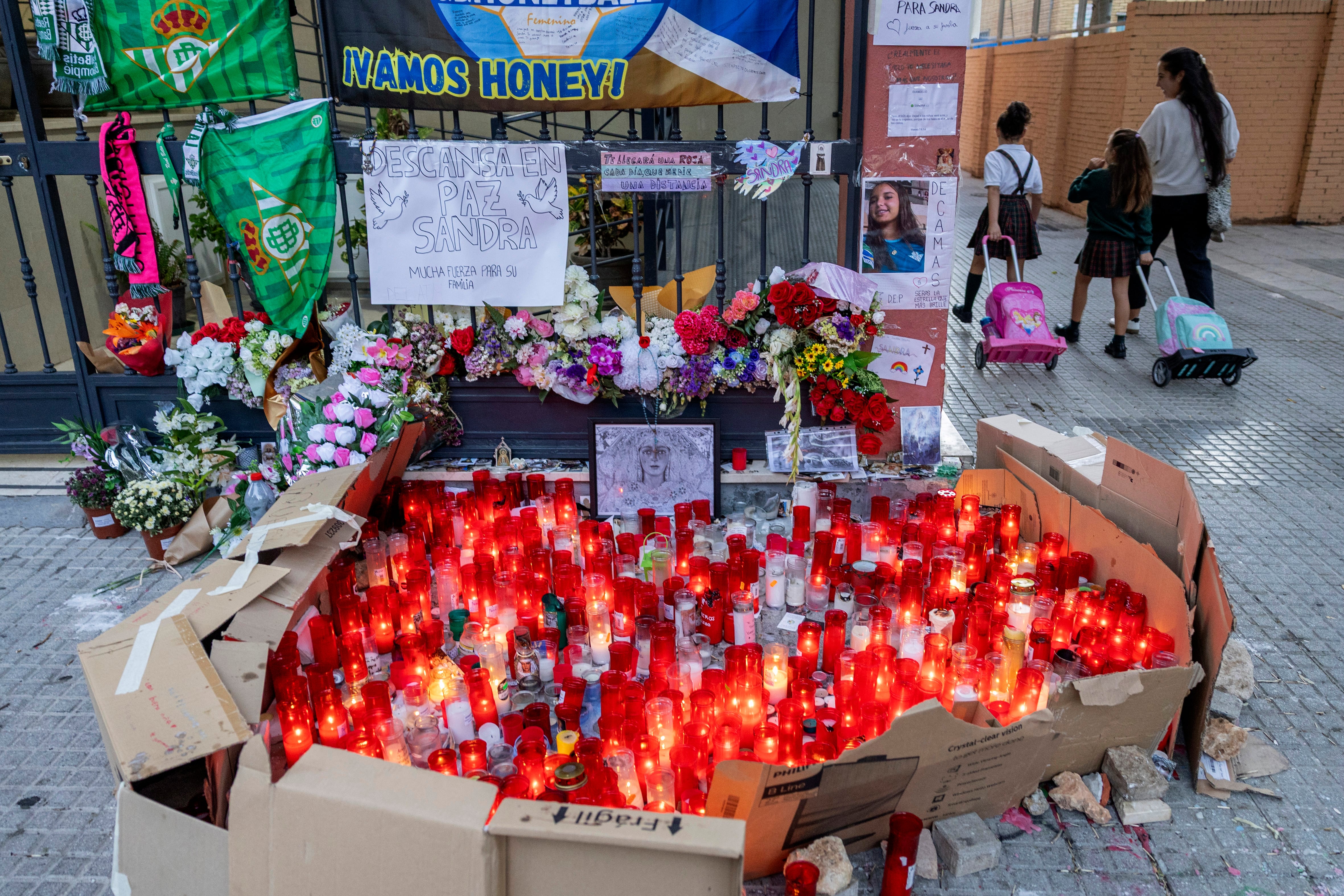 Alumnos del colegio Irlandesas de Loreto pasan junto a un altar de fotos, velas y flores en la puerta del domicilio de Sandra.