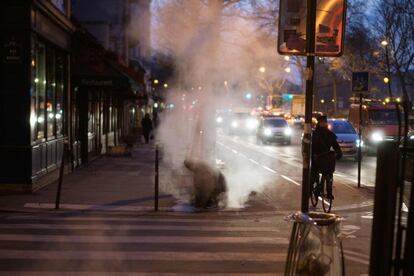 Un hombre se calienta con vapor en una calle de París (Francia).