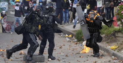 Dos policías corren para ayudar a un compañero que fue alcanzado con una bomba de gasolina durante una protesta en Bogotá, Colombia.