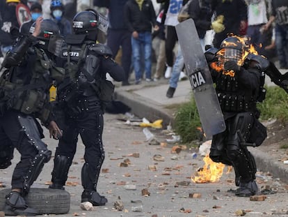 Dos policías corren para ayudar a un compañero que fue alcanzado con una bomba de gasolina durante una protesta en Bogotá, Colombia.
