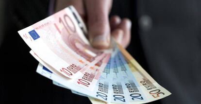 Una persona sostiene billetes de 10, 20 y 50 euros.