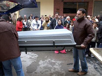 Unos operarios meten el féretro con el cadáver de Marta L.V, de 12 años, en un coche fúnebre ante numerosos vecinos.