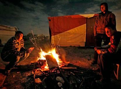 Tres hombres se calientan anoche con una hoguera en el poblado chabolista El Gallinero, en la Cañada Real.