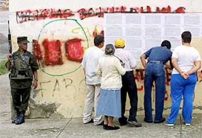 Un polica colombiano monta guardia mientras varios votantes buscan sus nombres en la lista electoral.