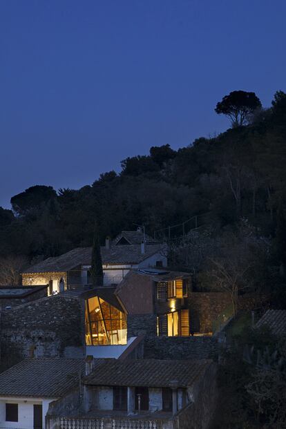 <p> Al anochecer, la intervención que de día ilumina el interior de la vivienda se convierte en una gran lámpara entre los tejados del pueblo. </p> <br> <p> Cambiar sin destrozar, crecer sin borrar. En Port de la Selva, un pueblo del Alt Empordà, de Girona, las arquitectas Nerea Calvillo y Marina Fernández Ramos — de C+arquitectos— deconstruyeron una antigua cuadra para construir una vivienda de vacaciones. Lo hicieron sin apenas rozarla porque el edificio estaba destrozado pero protegido. Uno de los forjados estaba roto y eso hacía la construcción, que no tenía ventanas, difícilmente habitable. </p> <p>Las proyectistas optaron por hacer explotar los patios de luz. Con cerramientos de vidrio inclinados para ampliar visualmente el espacio, los nuevos patios actúan como periscopios, la luz entra en la casa y con ella llegan las vistas a la Costa Brava. </p> <p> El nuevo forjado permite dividir en dos las actividades domésticas, y la organización abierta hace convivir usos y materiales. Hoy la piedra original acoge nuevas carpinterías metálicas y desde el interior de la antigua cuadra se puede ver el mar. </p>