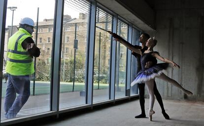 Un trabajador observa a los bailarines de ballet Brandon Brereton y Emily Pohl, que posan para una foto mientras comienzan los trabajos de construcción de un nuevo local en la Escuela Central de Ballet SE1, tras una exitosa campaña de recaudación de fondos, en Londres.