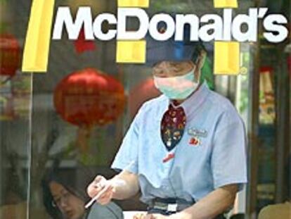 Una empleada de un restaurante de comida rápida sirve las mesas protegida con una mascarilla, como ordenan las autoridades chinas.