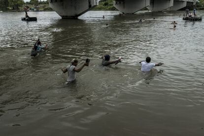 Un grupo de migrantes cruza el río Suchiate y carga sus zapatos en las manos para que no se mojen.