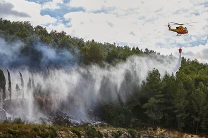 Un helicóptero lanza agua sobre las llamas del incendio forestal en Ador (Valencia), este sábado.