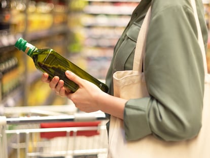 Una mujer compra una botella de aceite de oliva en un supermercado.