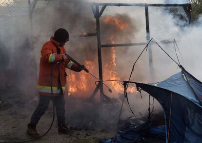 Un miembro del equipo de demolición extingue una tienda de campaña incendiada en 'La Jungla' de Calais. 