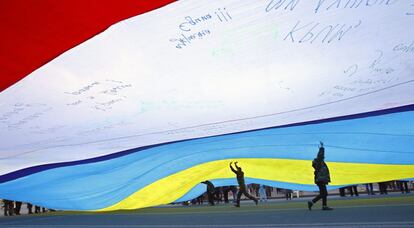 Varias personas caminan bajo una bandera gigante formadas con una bandera ucrania unida a una de Crimea, durante una protesta convocada en la Plaza de la Independencia de Kiev, Ucrania.