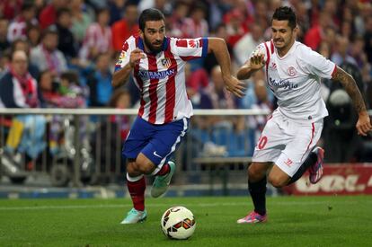 Arda Turan, del Atl&eacute;tico, y el sevillista Vitolo Mach&iacute;n se disputan un bal&oacute;n. 