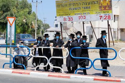 Un grupo de judíos ultraortodoxos, llevan máscaras protectoras debido a la pandemia, se reúnen a la entrada de un barrio que ha quedado aislado tras el reciente aumento de los casos de coronavirus en la ciudad costera de Ashdod, en Israel.